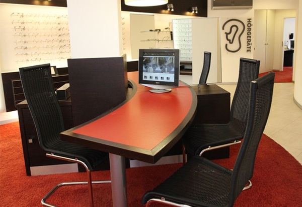 Modernes Hörgeräte-Fachgeschäft mit Beratungstisch, Bildschirm und Brillenauswahl.